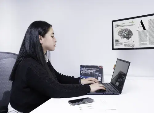 Mujer trabajando en un portátil con un monitor adicional que muestra una ilustración del cerebro.