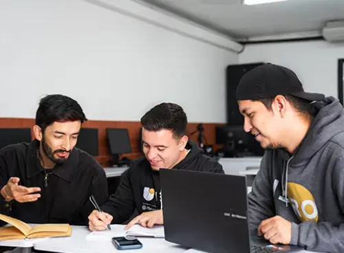 Varias personas en una reunión: una con un computador al frente, otra firmando un documento y otra hablando.