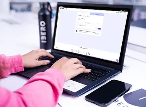 Persona frente a un portátil con una encuesta en pantalla; al lado hay un celular y un termo.