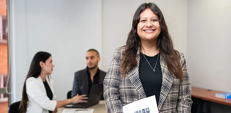 mujer joven en primer plano mirando a la cámara y de fondo dos personas conversando